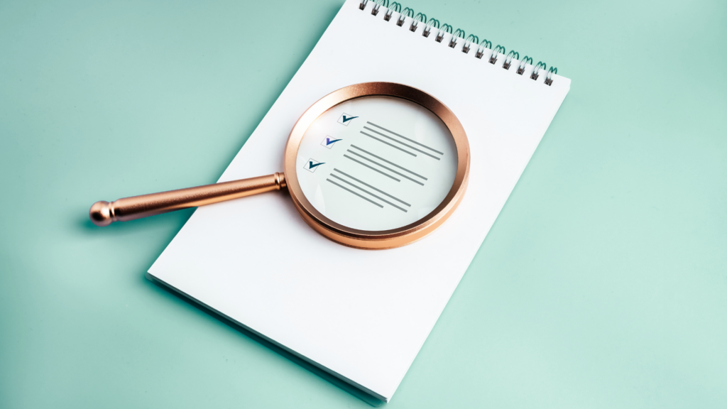 Copper magnifying glass over a checklist with three checked items on a white spiral notebook.